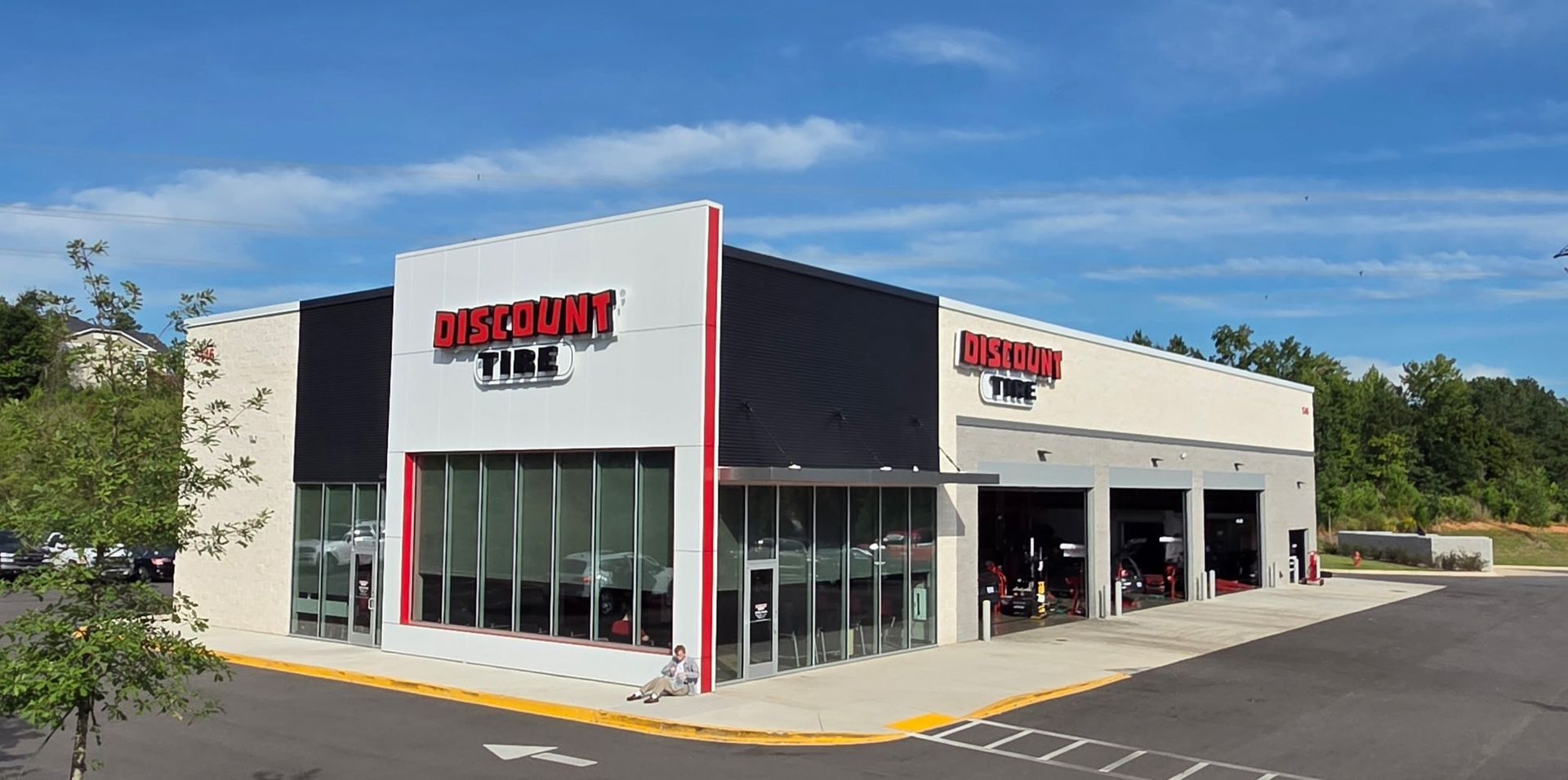 Exterior of a Discount Tire store with glass windows and a red-and-white sign on a sunny day