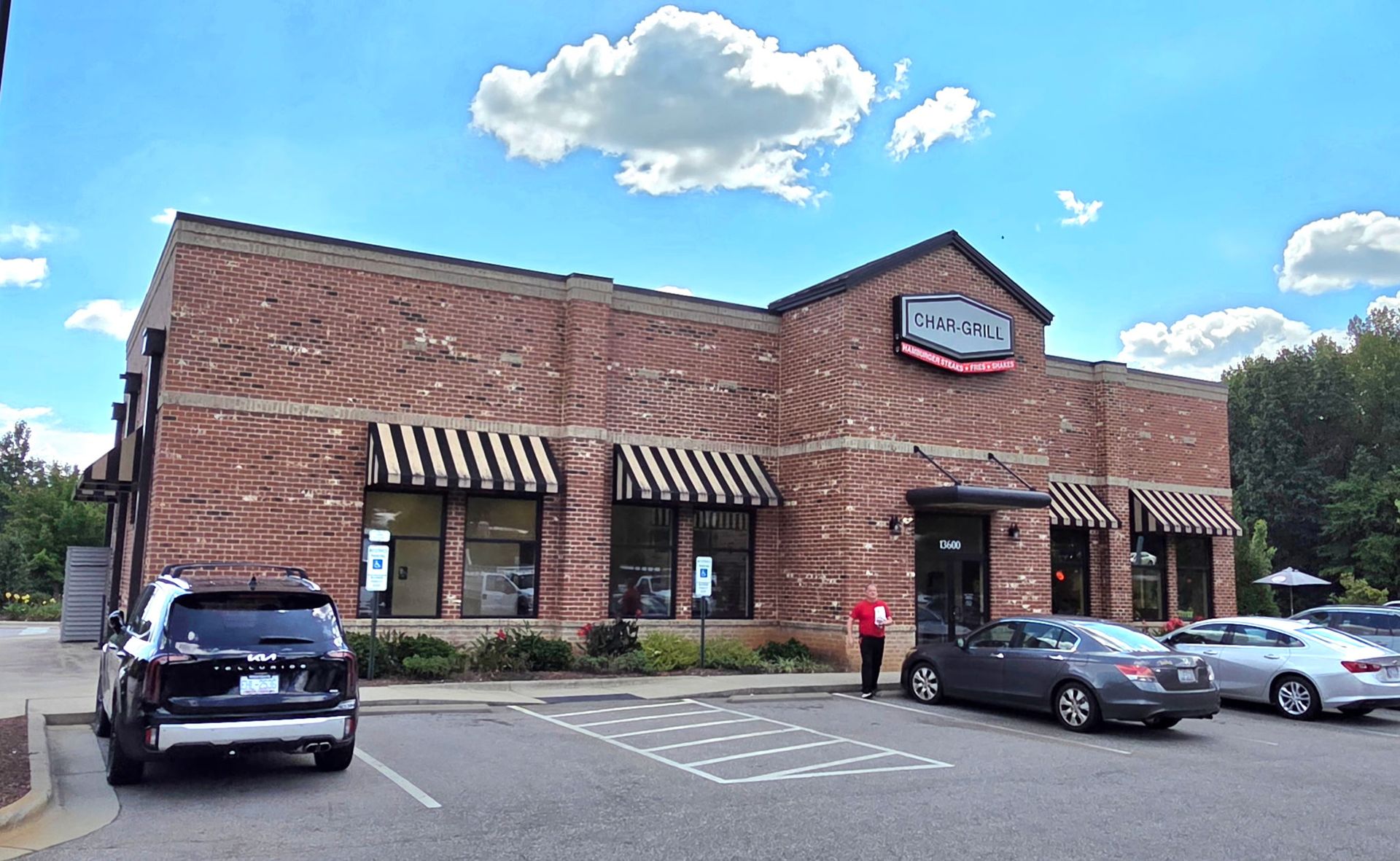 Brick storefront with striped awnings and parked cars under a blue sky with clouds
