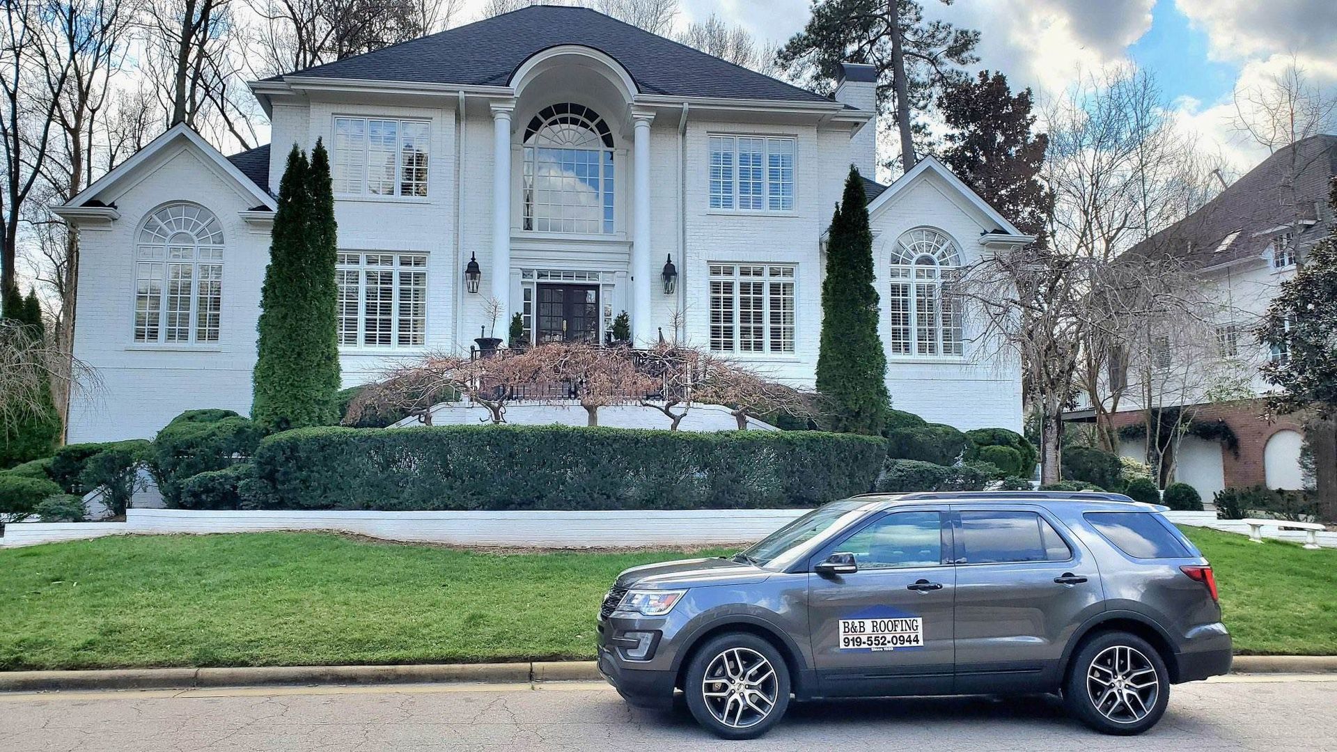 Grey SUV parked in front of a large white house with trimmed landscaping and trees in Apex, NC.