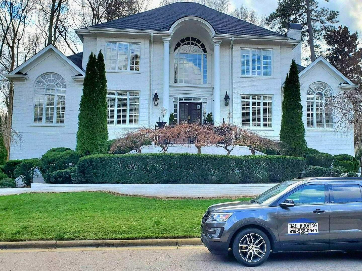 A car is parked in front of a large white house.