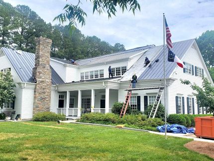 A large white house with a metal roof is being remodeled.