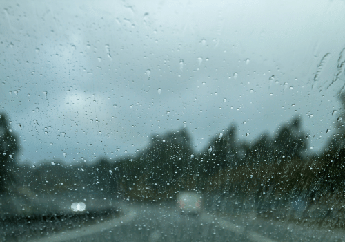 Rain-speckled windshield on a blurred road with trees and car headlights in the distance