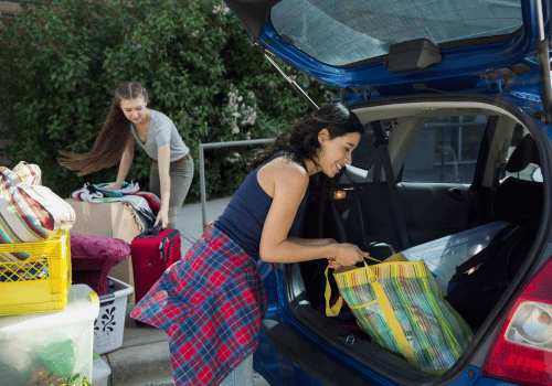 People loading colorful bags and luggage into a blue car outdoors