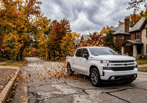 White Chevrolet Silverado driving through falling autumn leaves on a residential street
