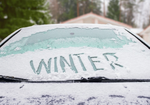 Snow-covered car windshield with “WINTER” written in the frost