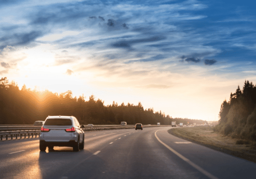 Car driving on a curving highway at sunset with trees lining both sides