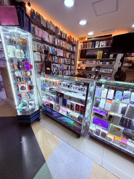 Interior de una pequeña tienda con vitrinas de cristal y estantes llenos de artículos coloridos bajo luces cálidas.