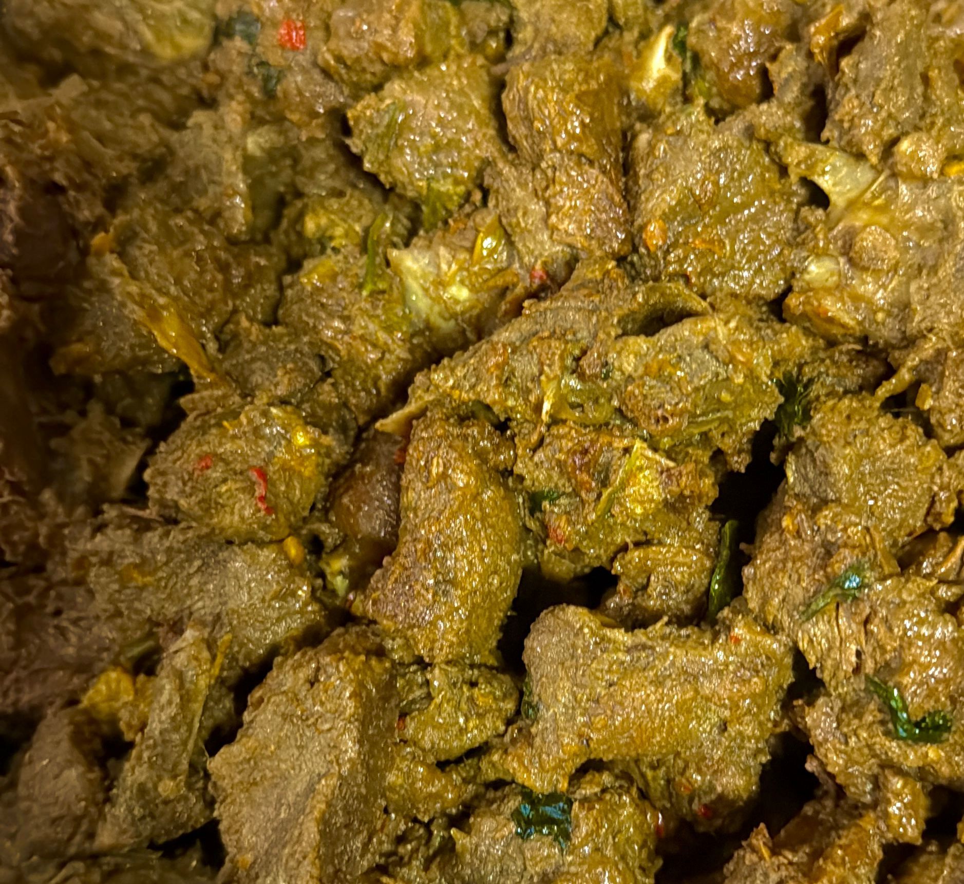 Close-up van een gerecht met bruine, gestructureerde stukjes vlees bedekt met een groen-gele kruidenpasta.