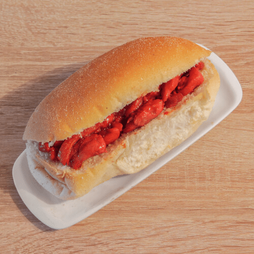 Een sandwich op een wit dienblad, brood gevuld met rood vlees, rustend op een houten tafel.