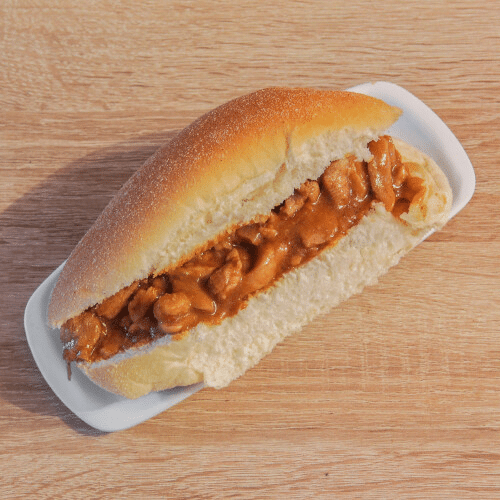 Een sandwich met bruine vulling op een wit bord, geplaatst op een houten ondergrond.