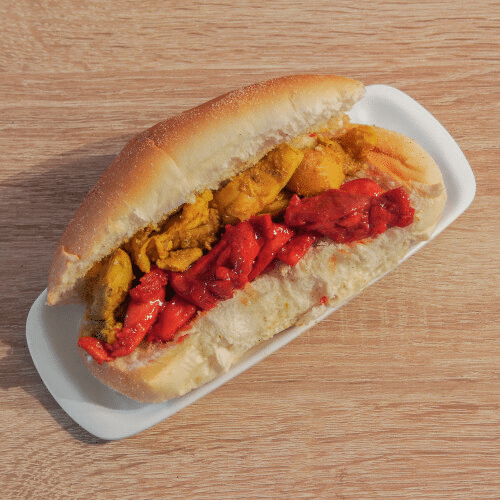 Sandwich met gele en rode vulling op een wit bord, met een houten achtergrond.