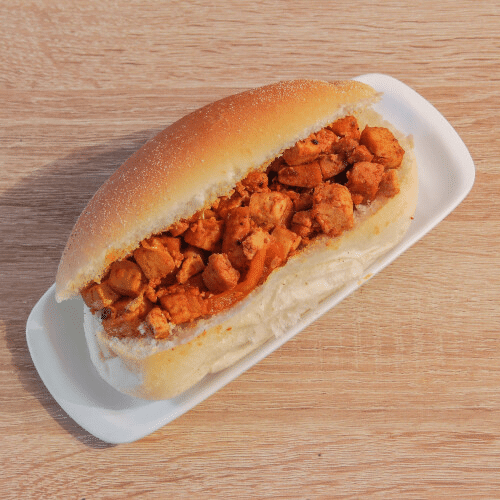 Kipsandwich op een wit bord, geserveerd op een lichtbruin broodje, met rode saus.