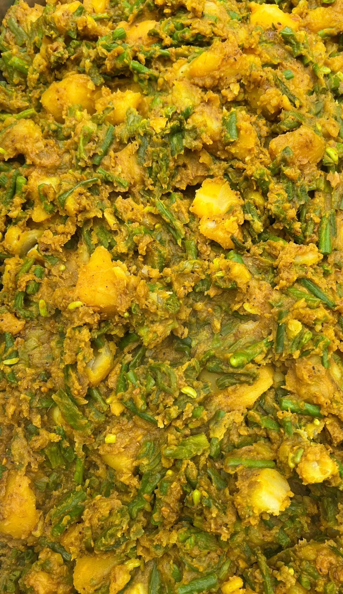 Een gerecht met geelachtige Indiase curry, waarin sperziebonen, aardappelen en kruiden zichtbaar zijn.