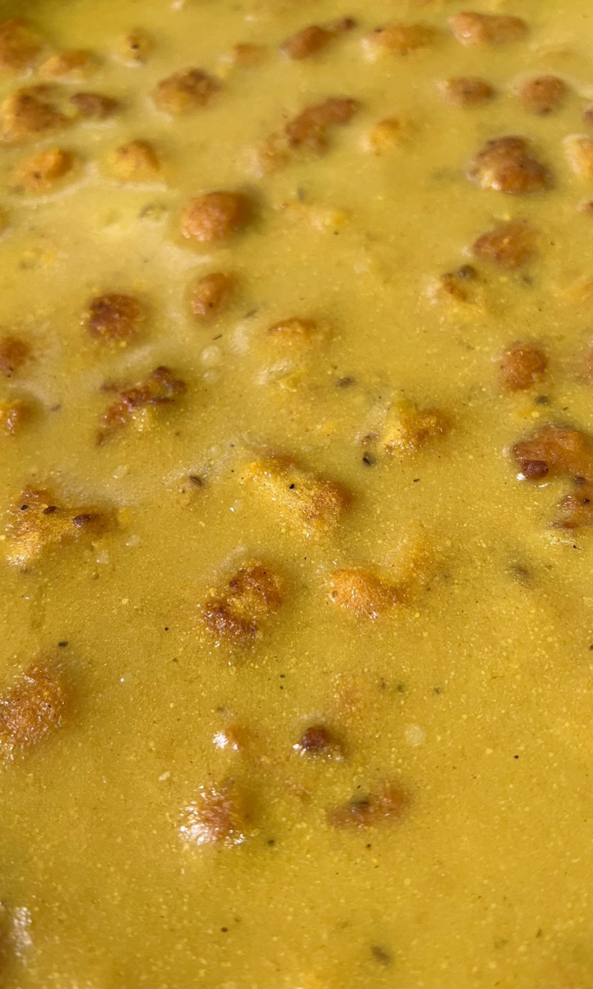 Close-up van een geel-oranje soep met kleine, goudbruine croutons die op het oppervlak drijven.
