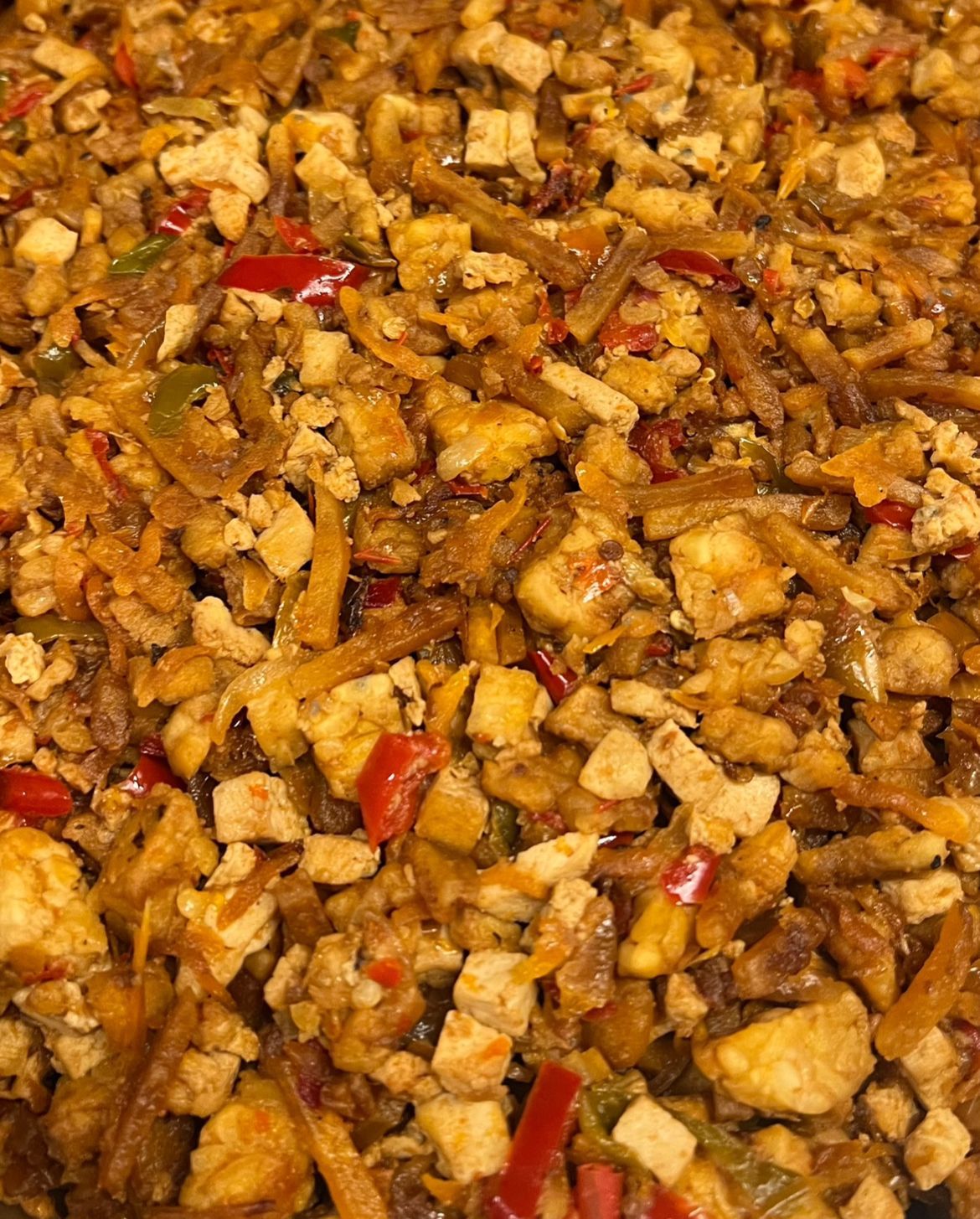 Close-up van een gemengd roerbakgerecht met kipblokjes, rode en groene paprika's en bruine noedels.