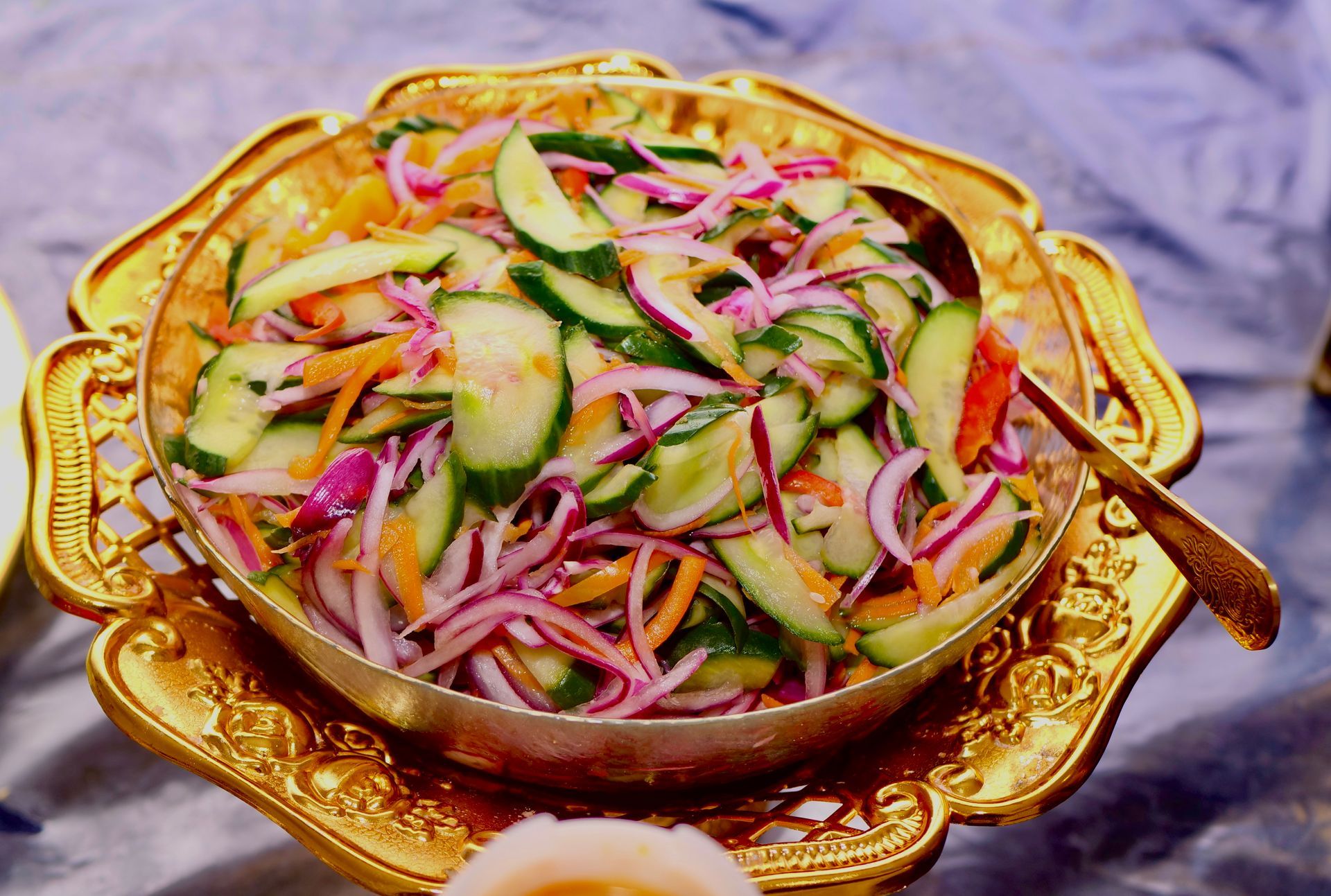 Salade van gesneden komkommer, rode ui en wortelen in een gouden sierkom.