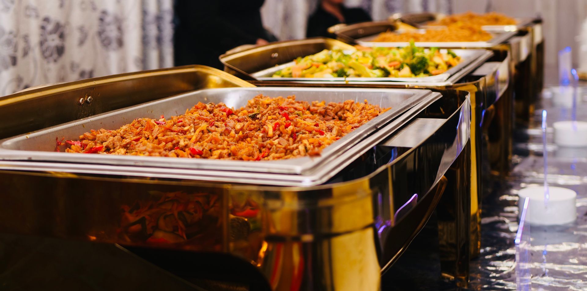 Buffet met diverse gerechten in gouden warmhoudschalen, opgesteld op een lange tafel.