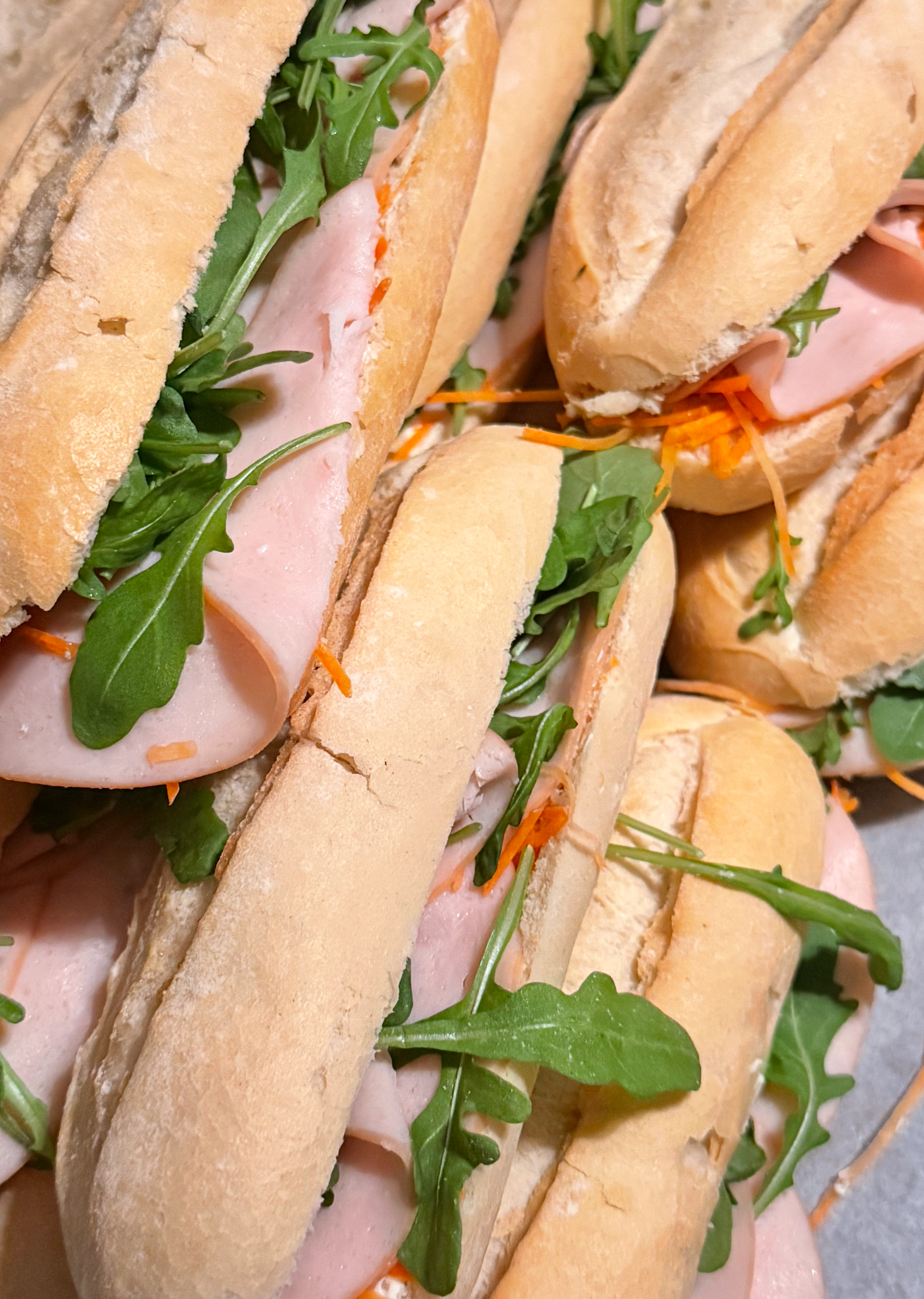 Sandwiches op een schaal: ham, rucola en wortelreepjes in halve stokbroden.
