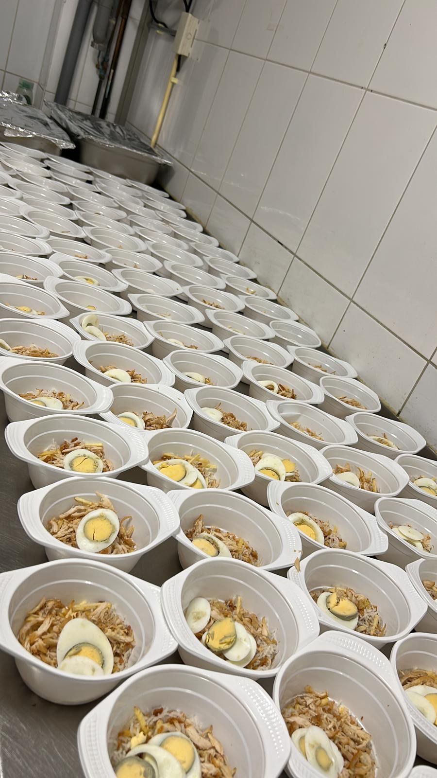 Rijen witte kommen gevuld met eten en gesneden hardgekookte eieren in een keuken.