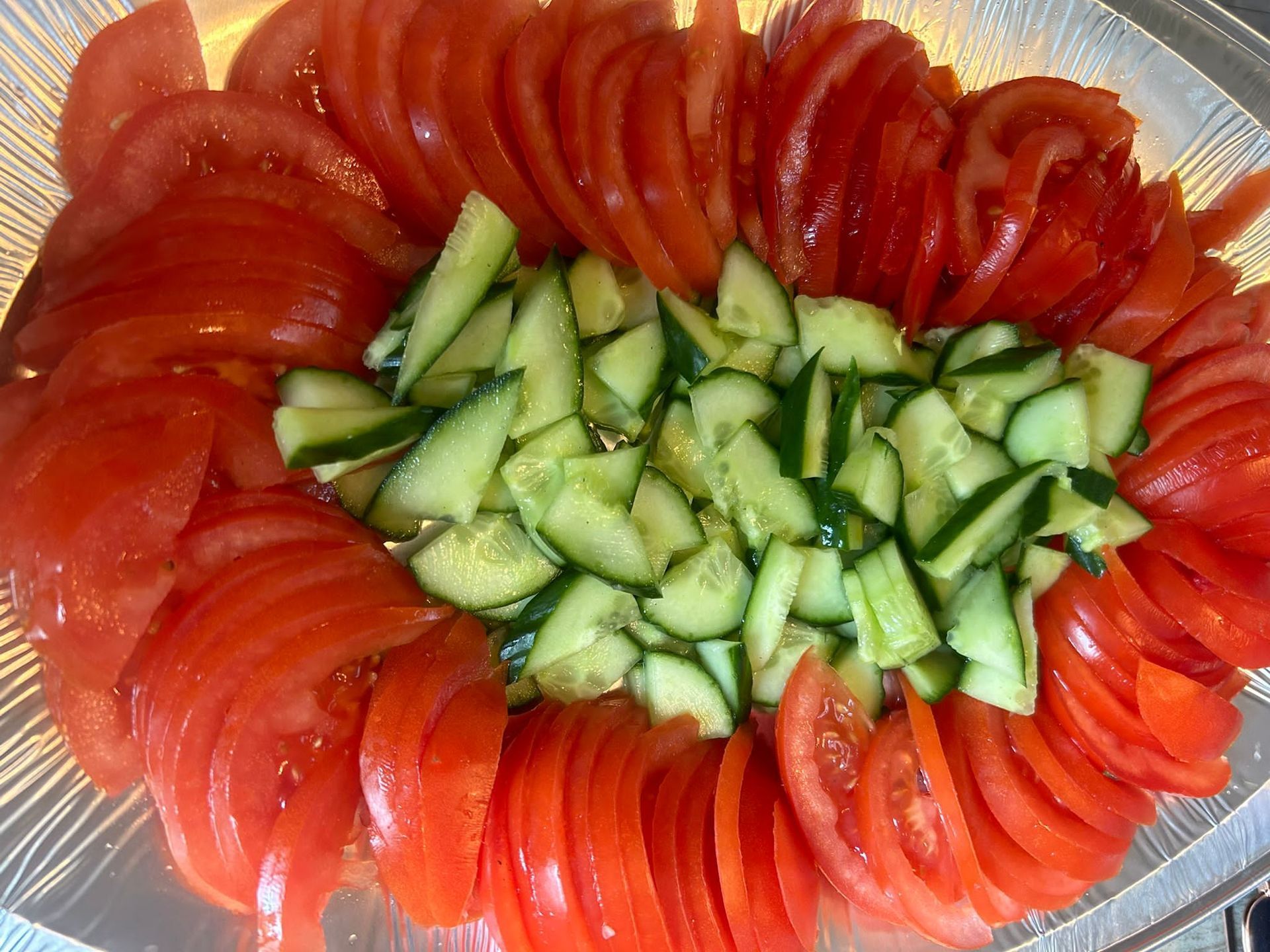 Gesneden tomaten en in blokjes gesneden komkommers op een doorzichtige schaal.