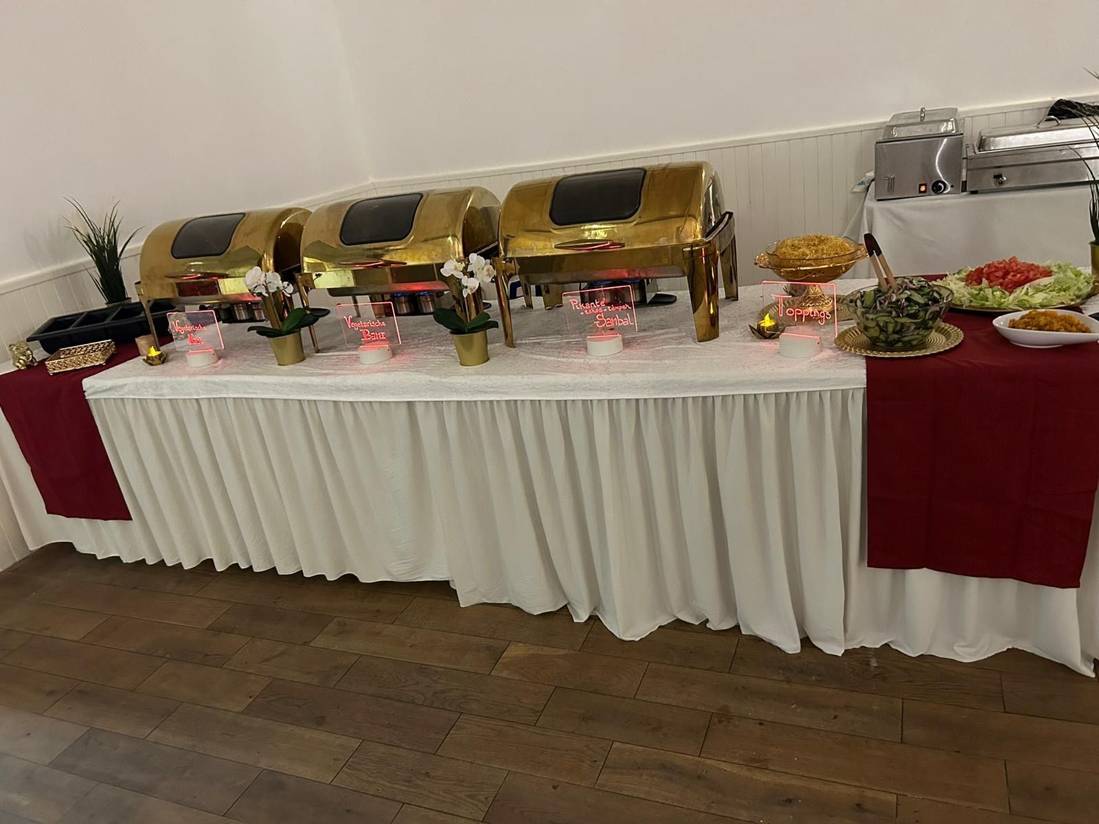 Buffettafel met gouden warmhoudschalen, diverse gerechten en bordeauxrode accenten.