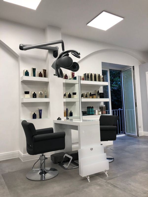 Modern hair salon with black styling chairs, shelves of products, and a wall-mounted hair dryer