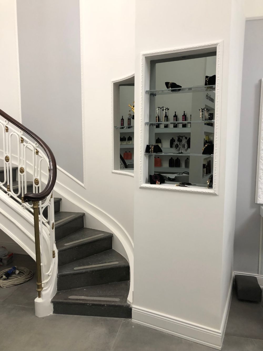 Curved staircase with dark carpet and white banister beside a mirrored wall niche in a bright interior