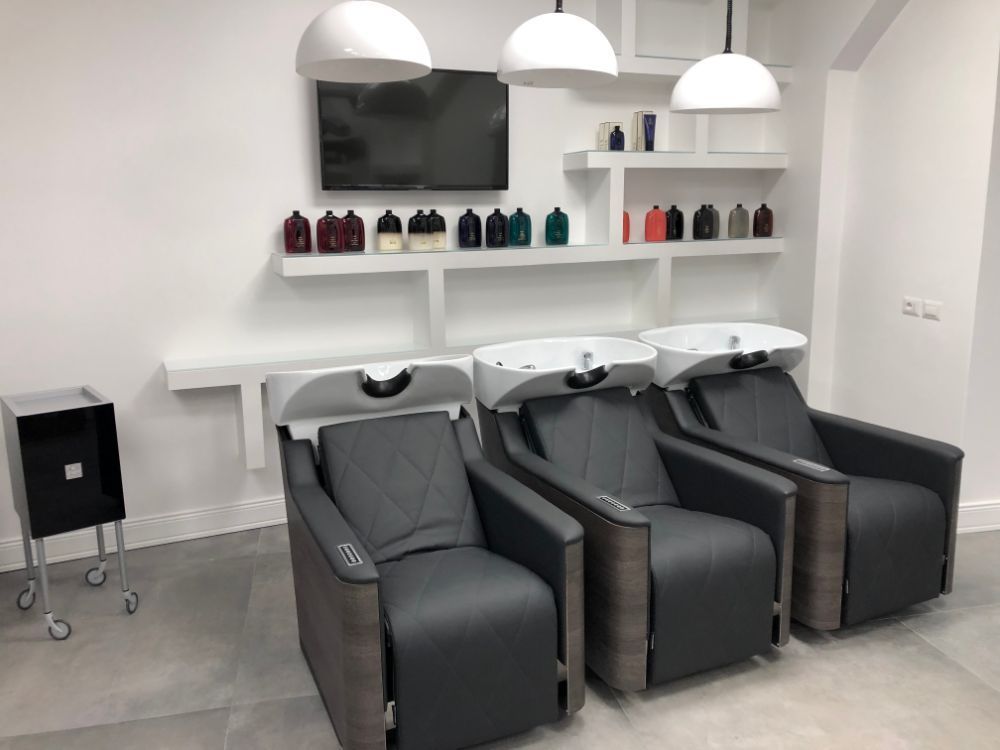 Modern hair salon with three black wash chairs, white shelves, and hanging dome lights