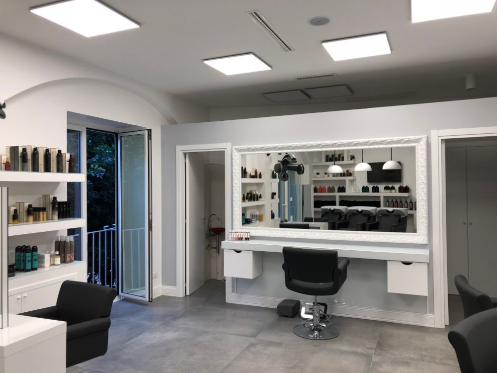 Bright modern salon with styling stations, mirrors, shelves, and a black chair under white ceiling lights