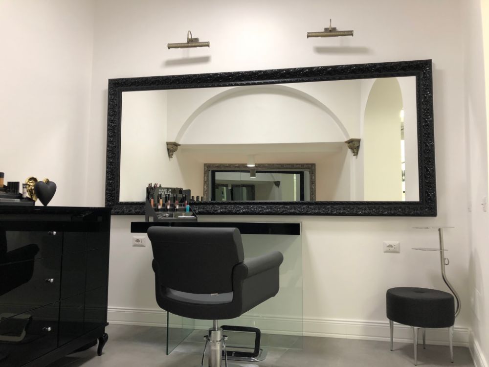 Salon station with black styling chair, large mirror, and small black side table against white walls
