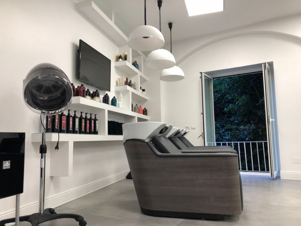 Modern salon interior with styling chairs, mirrors, shelves of products, and an open doorway to a balcony.