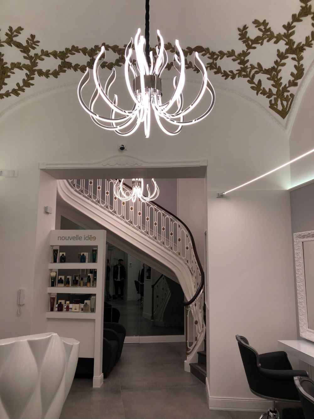 Elegant white interior with a spiral staircase, chandelier, and decorative vine trim above the doorway.
