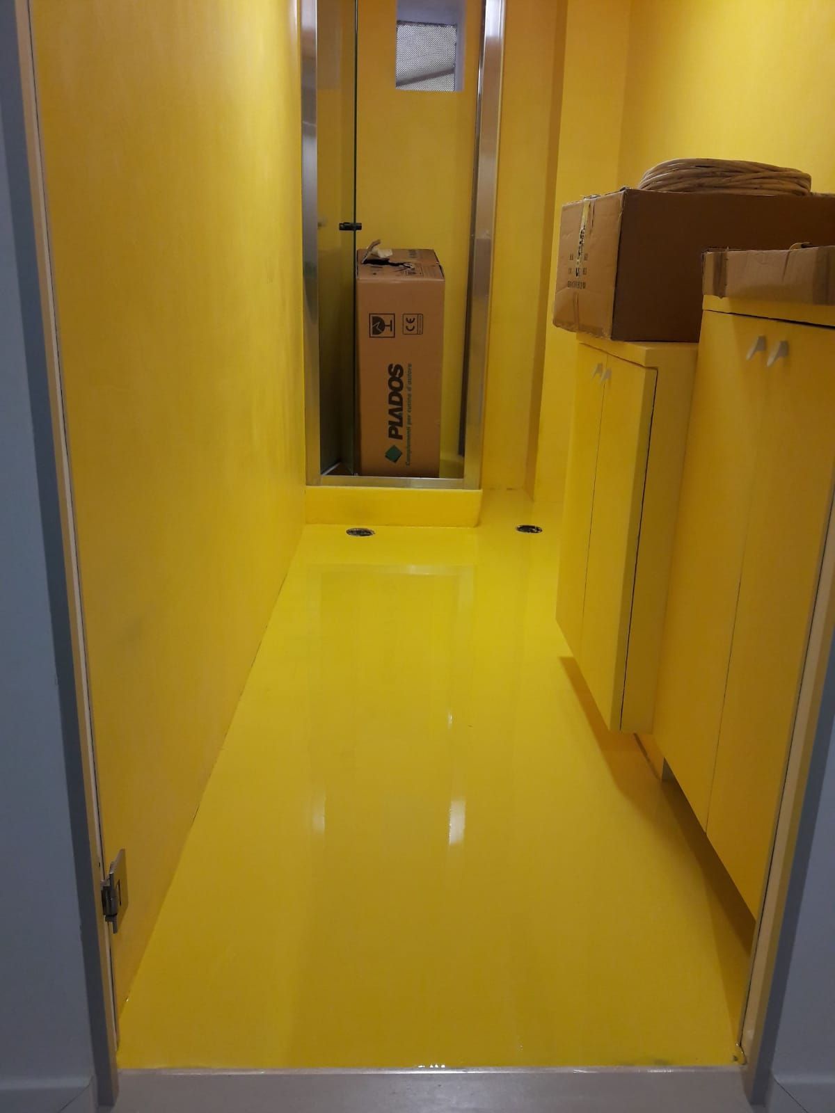 Yellow hallway with glossy floor and cabinets, leading to a cardboard box at the far end.