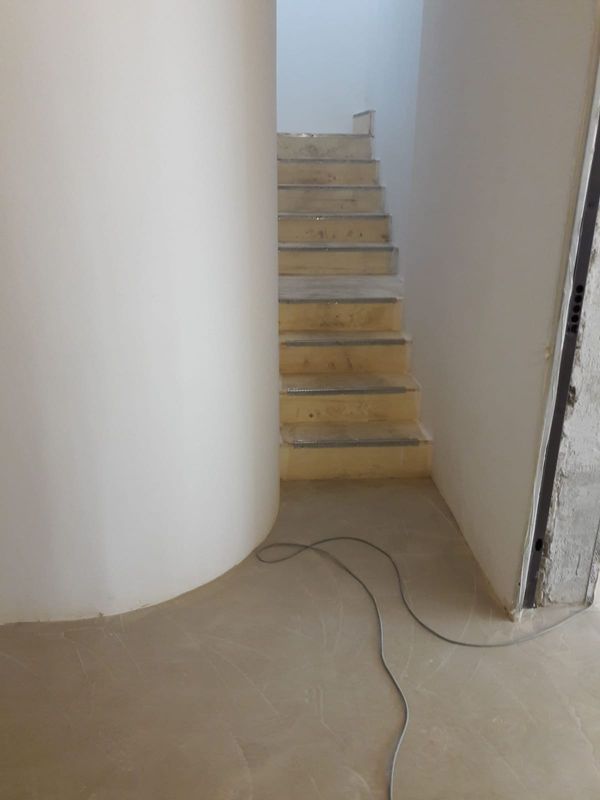 Narrow indoor stairway with beige steps between white walls and a cable on the floor