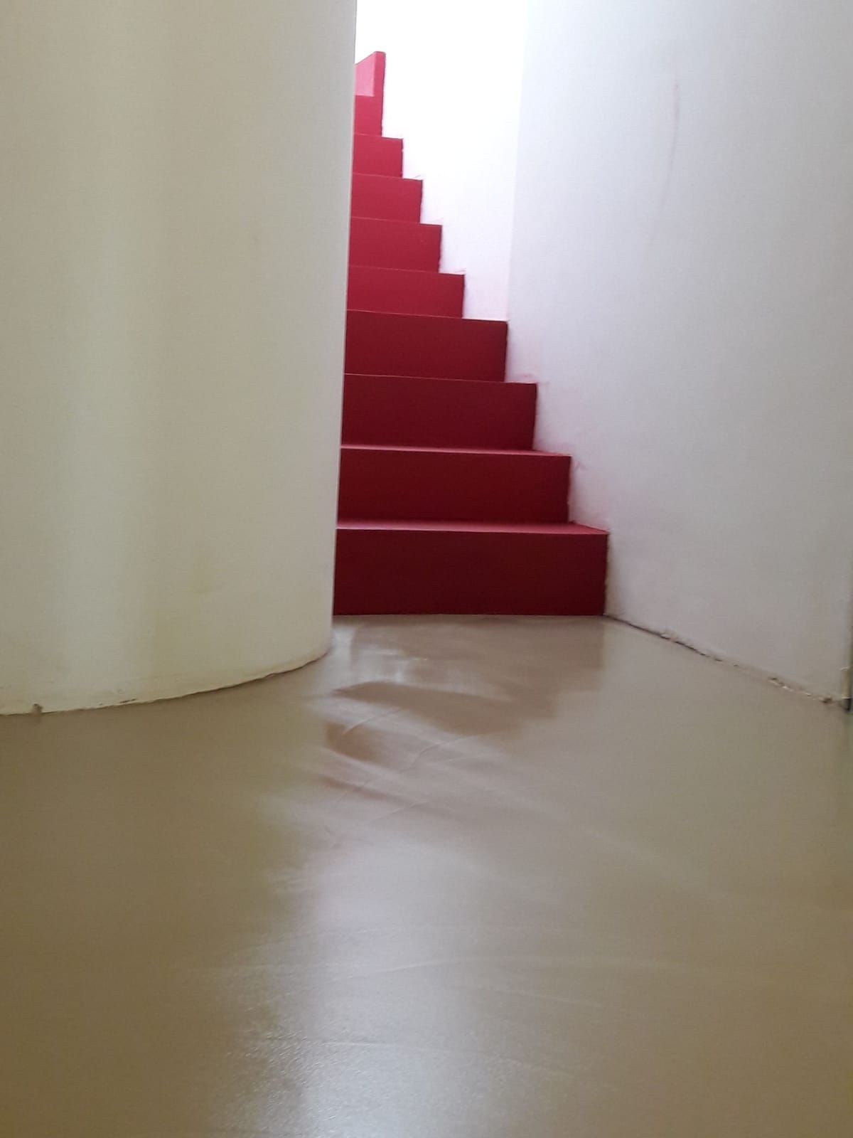 Red staircase between white walls with a curved white column and beige floor.