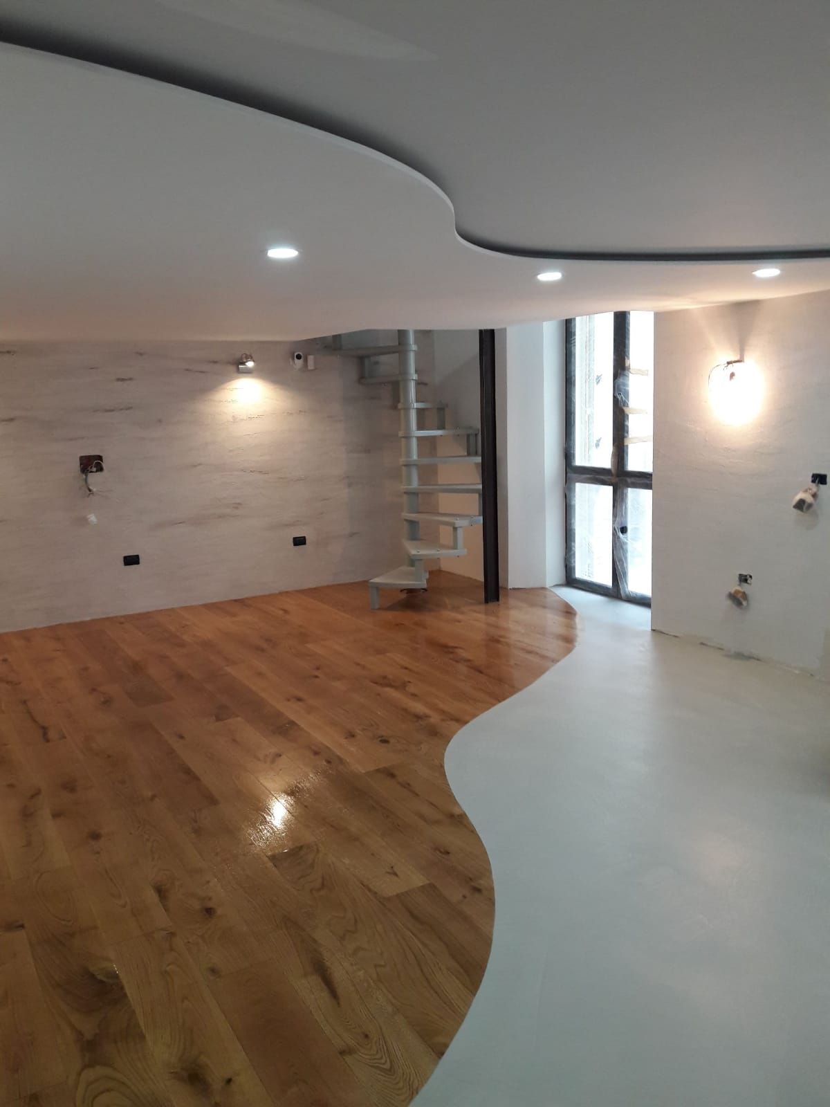 Empty modern room with curved white ceiling, wood floor, built-in lights, and glass door by a brick staircase