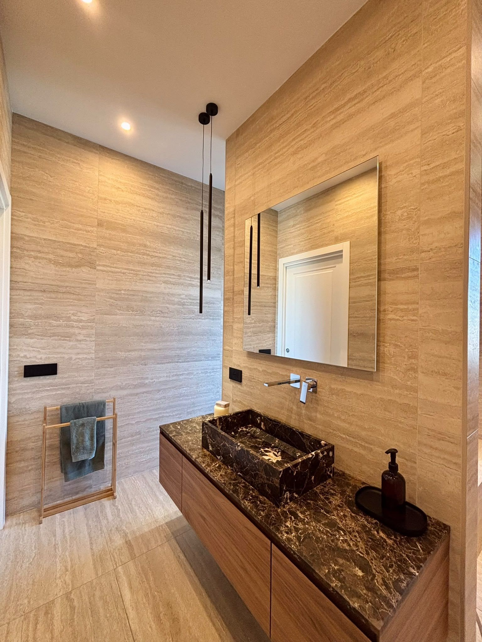 Modern beige bathroom with black countertop, wall mirror, sink, and toilet paper holder.