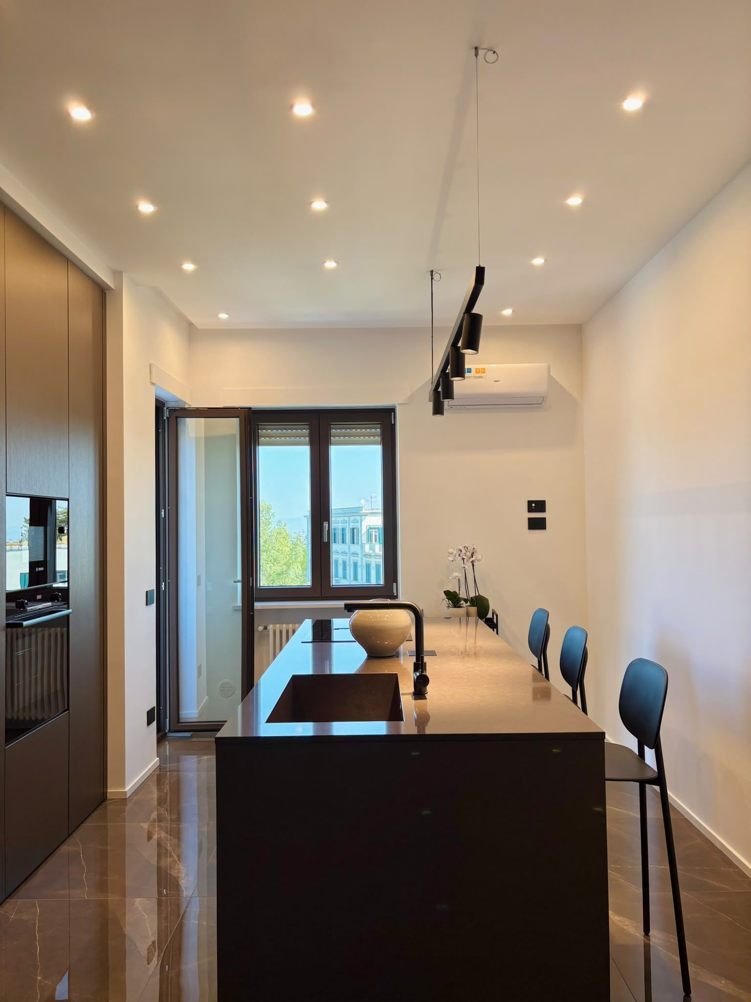 Modern kitchen with dark island, bar stools, pendant lights, and large windows overlooking a city view