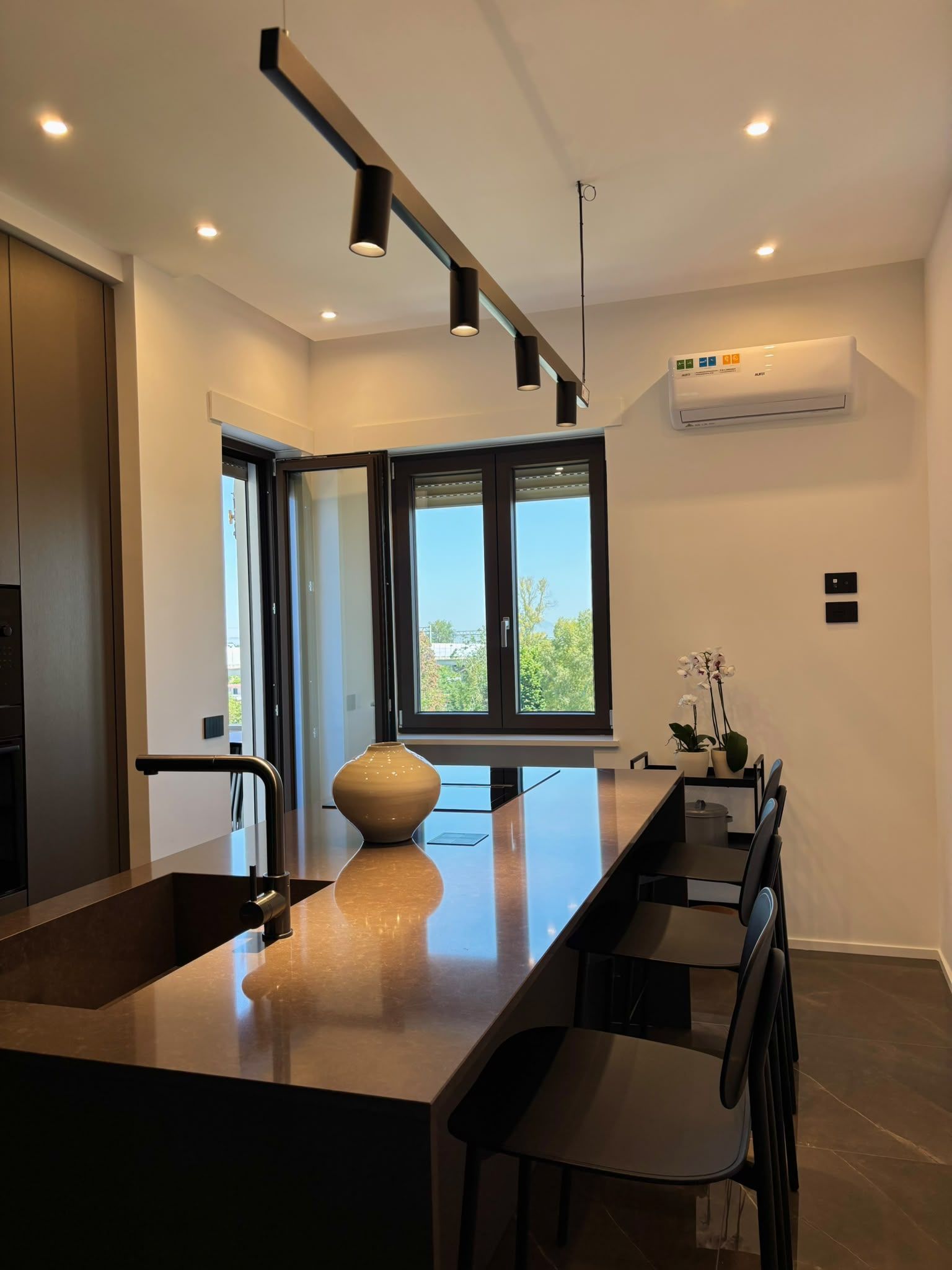 Modern dining room with glossy black table, pendant lights, large windows, and a wall-mounted air conditioner