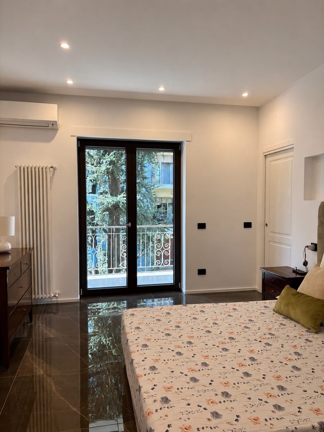 Bright bedroom with balcony doors, white walls, recessed lights, and a patterned bedspread.