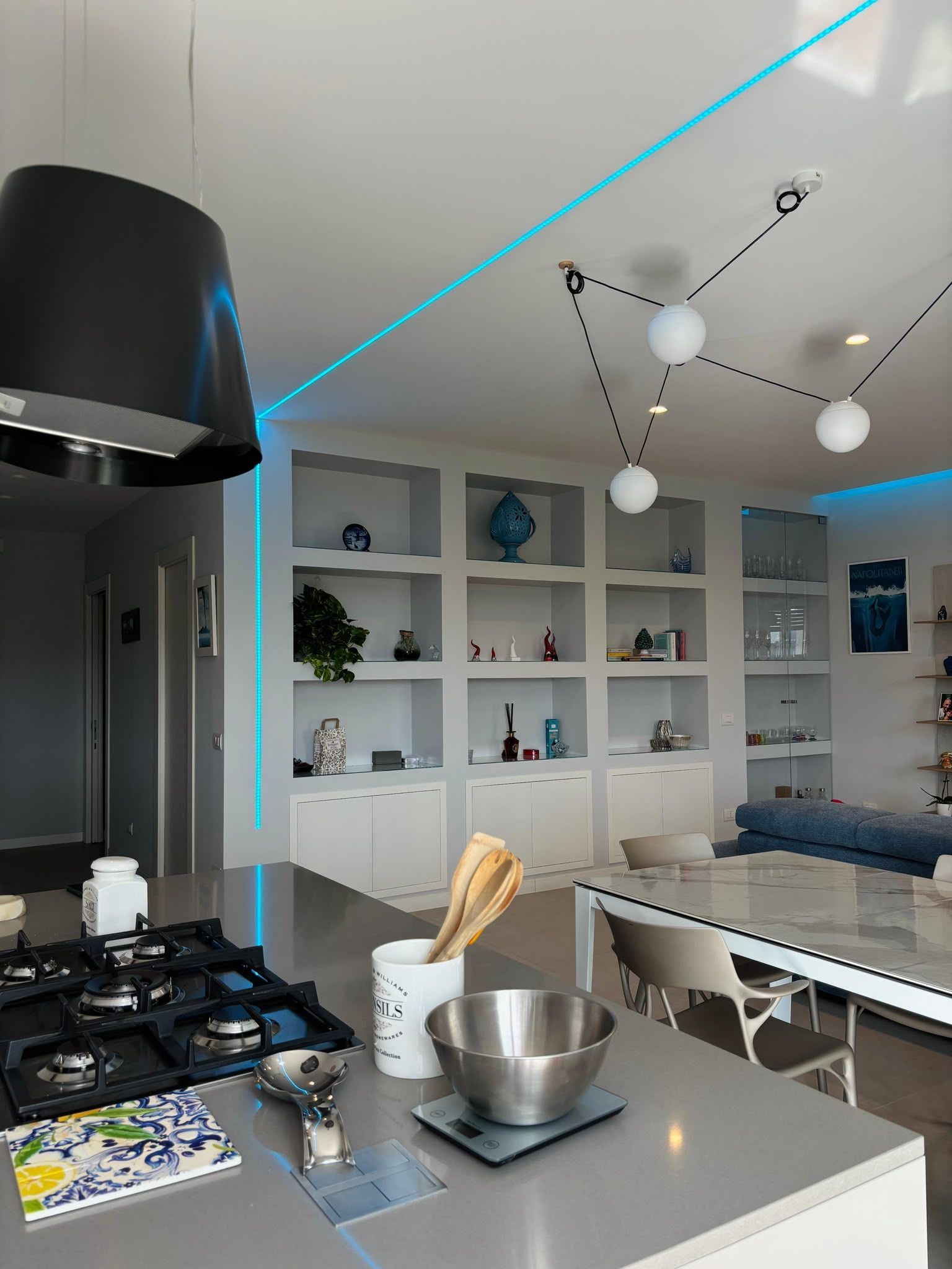 Modern kitchen with gas stove, gray island, built-in shelves, and blue LED ceiling lights