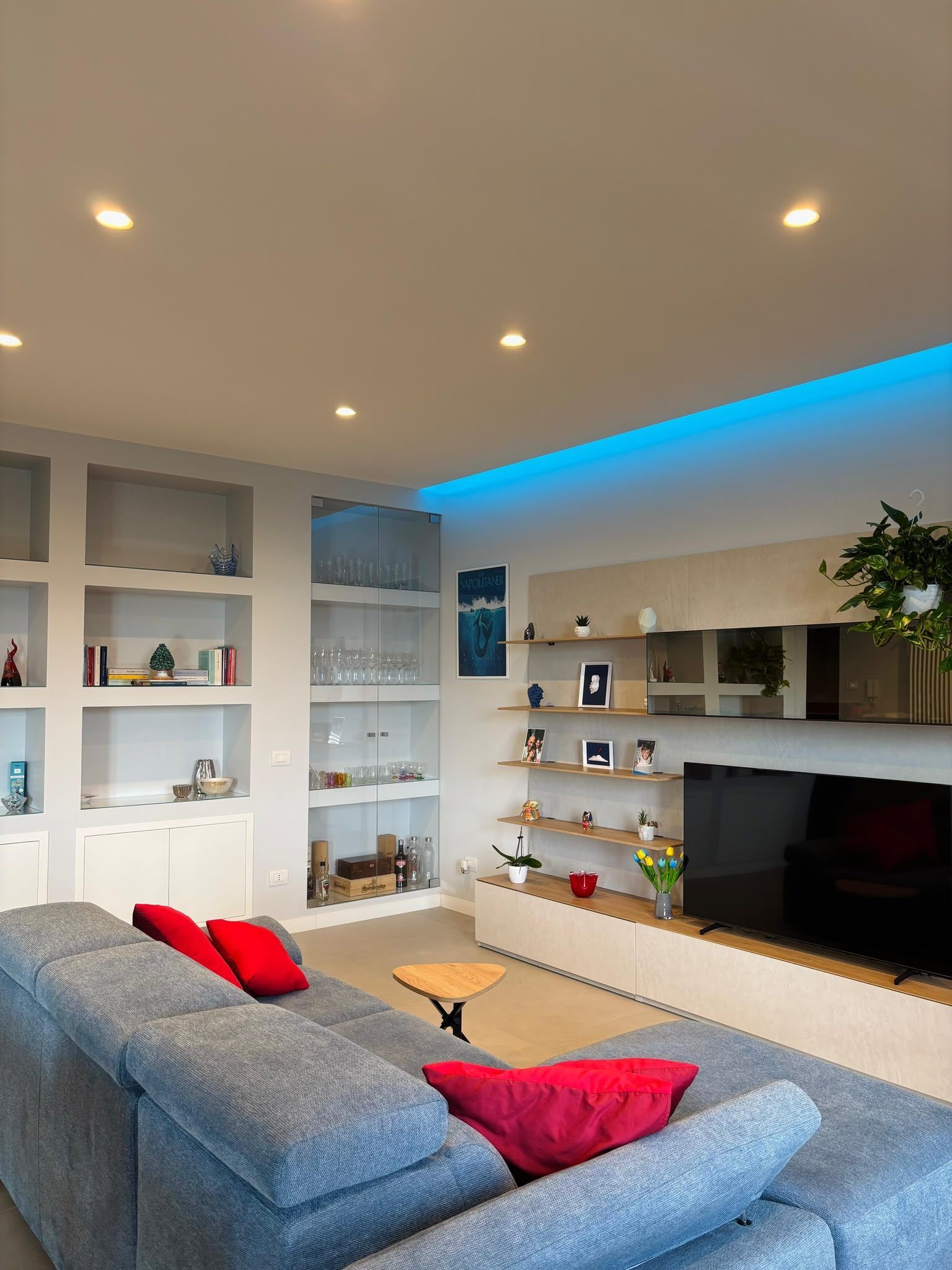 Modern living room with blue sofa, white shelving, and a TV wall with blue LED lighting