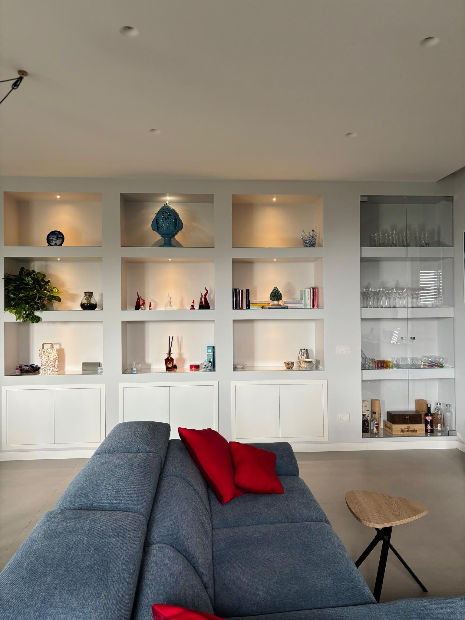 Modern living room with built-in white shelves, decorative objects, and a blue sofa with red pillows.