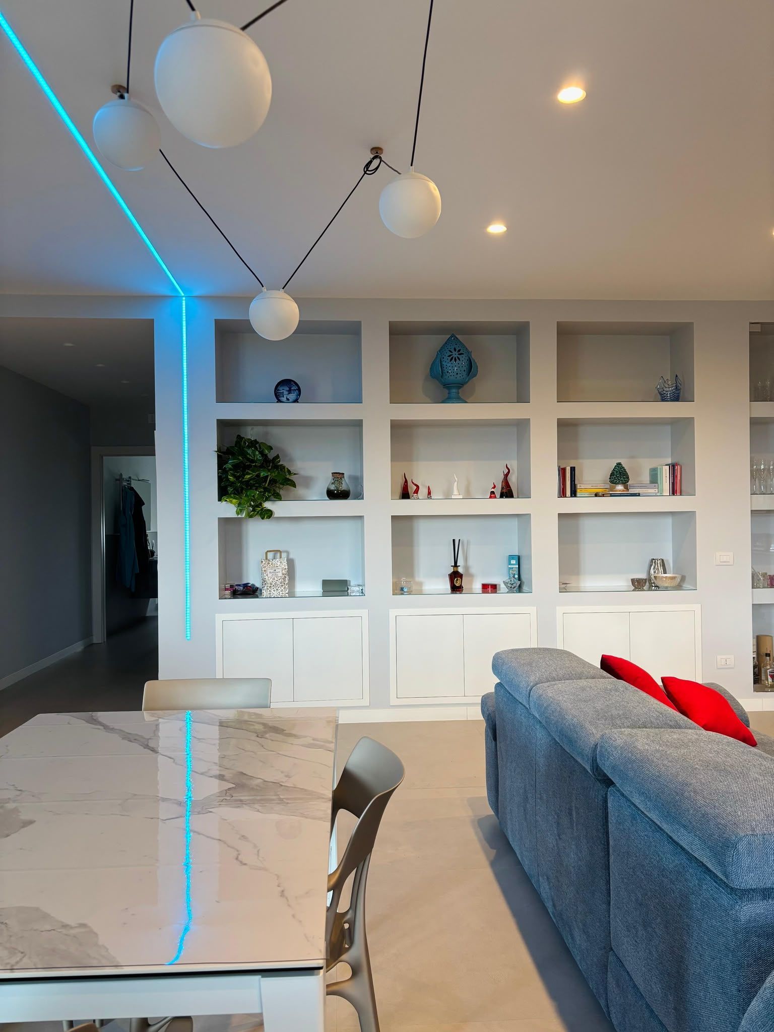 Modern living room with built-in shelves, blue sofa, marble table, and hanging globe lights