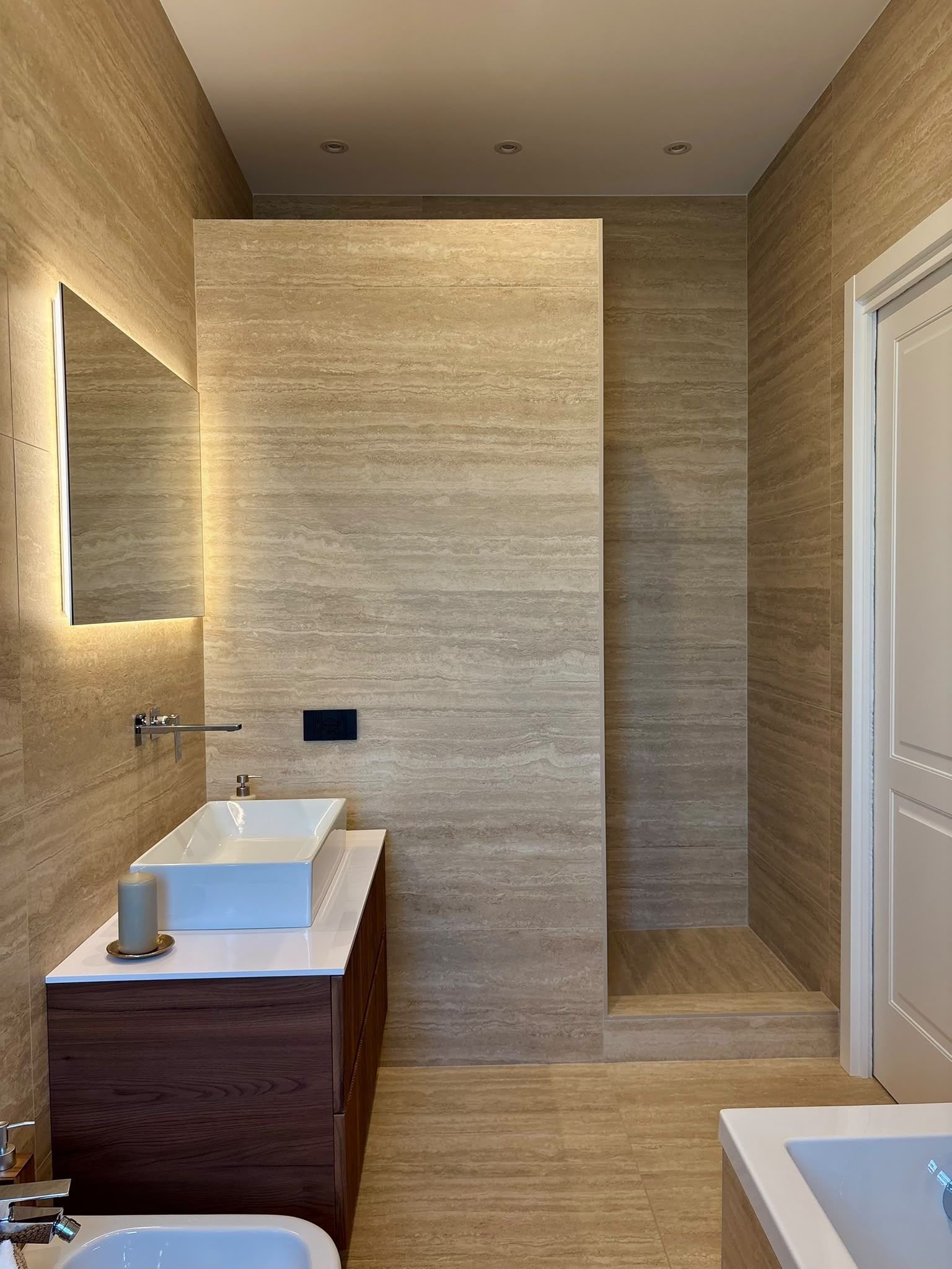 Modern bathroom with beige textured walls, wood vanity, wall mirror, and white tub.