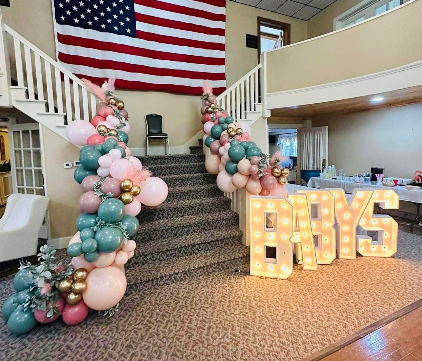 Staircase decorated with green, pink, and gold balloons, with large light-up letters spelling