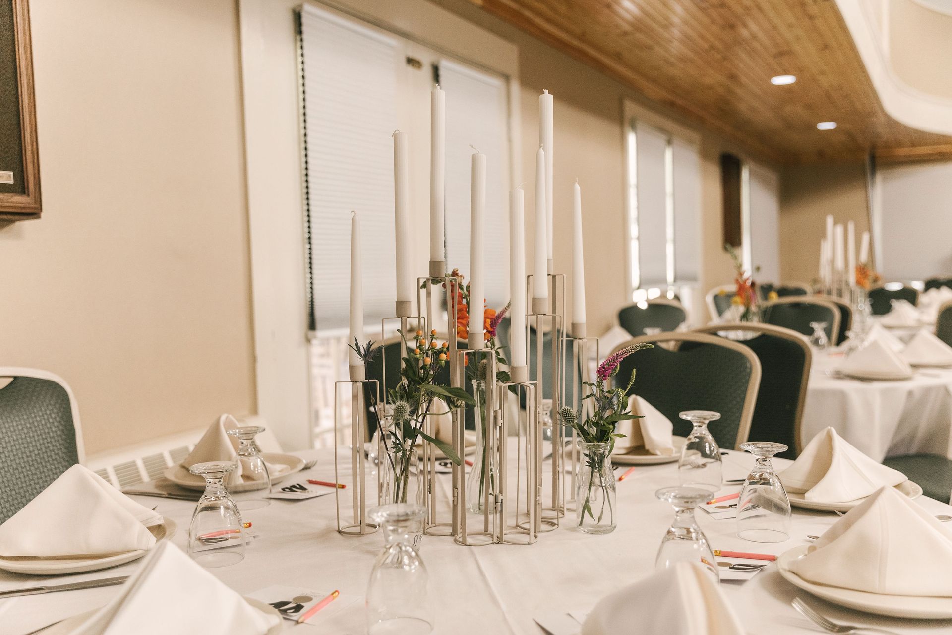 A formal table setting features a central metallic candelabra with white candles, surrounded by white linens and glassware.