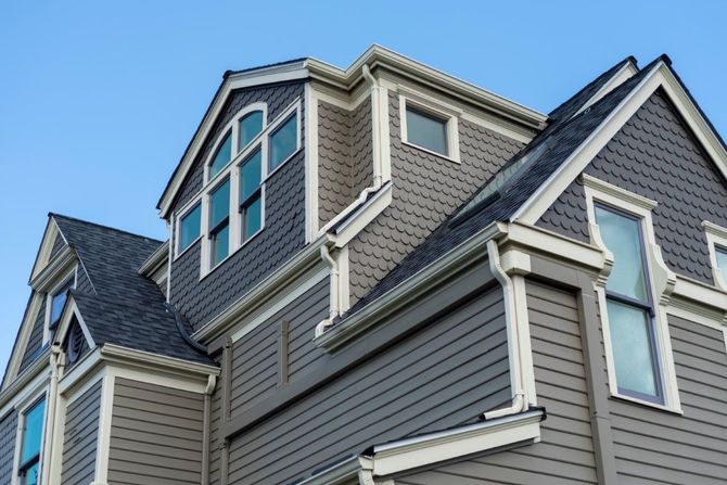 Gray Victorian house exterior with white trim and blue bay windows against a blue sky