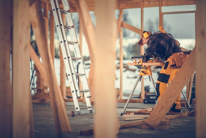 Construction workers fitting wooden beams inside a house under renovation, with ladders and tools nearby.