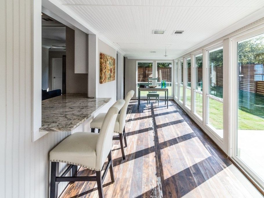 Bright sunroom with glass doors, chairs, and striped floor rug overlooking a green backyard